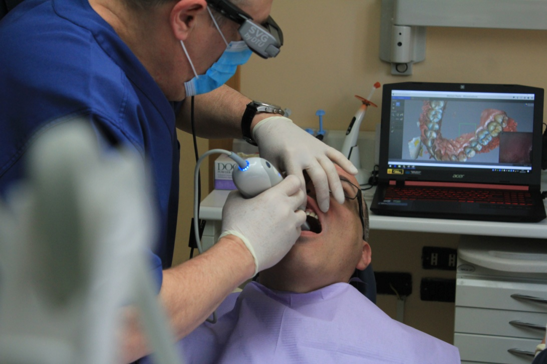 A dentist using a device with a camera to project a patient's teeth on a computer