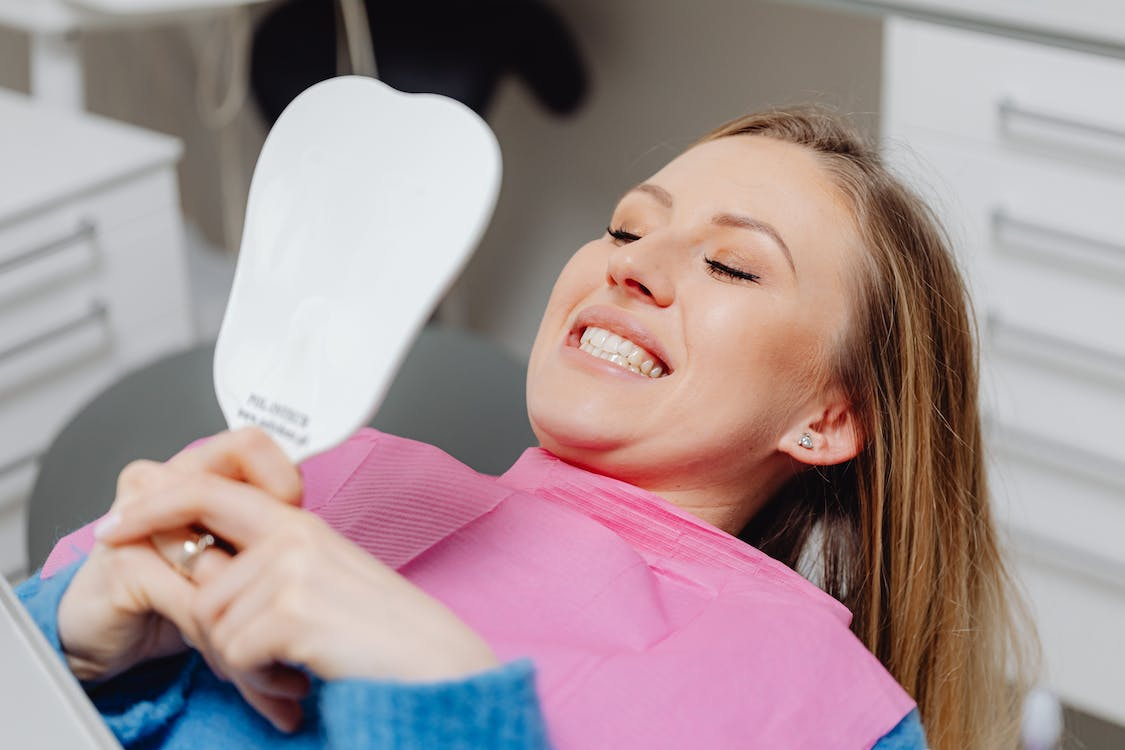 A person smiling while looking in a handheld mirror